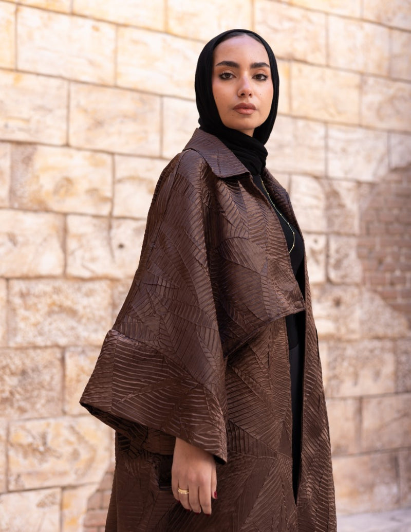 Woman wearing a brown textured coat against a stone wall.