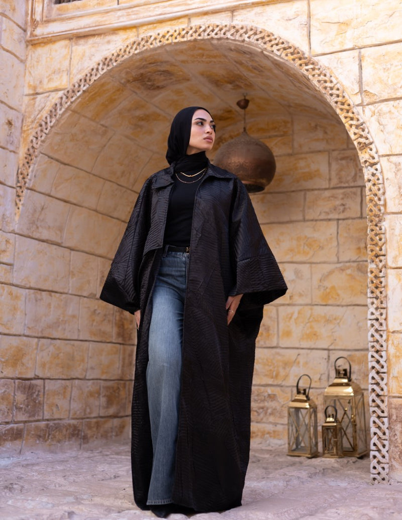 Woman in a black abaya standing in front of an archway with stone walls.