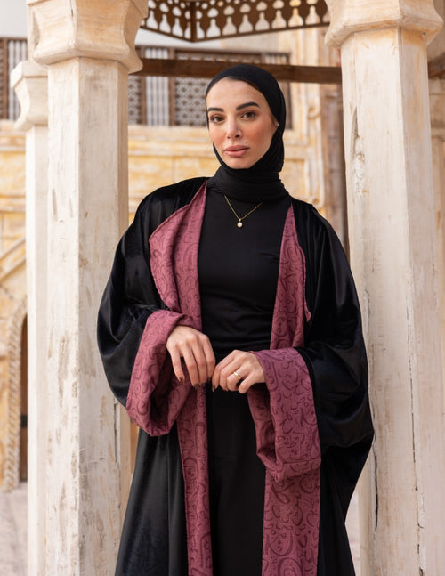 Woman wearing a black abaya with a maroon scarf in an architectural setting