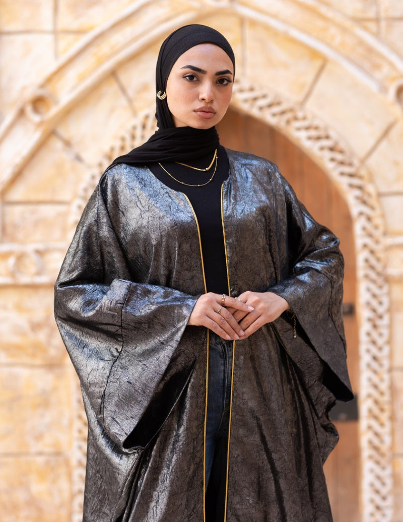Woman wearing a metallic abaya with a black hijab in front of an architectural background
