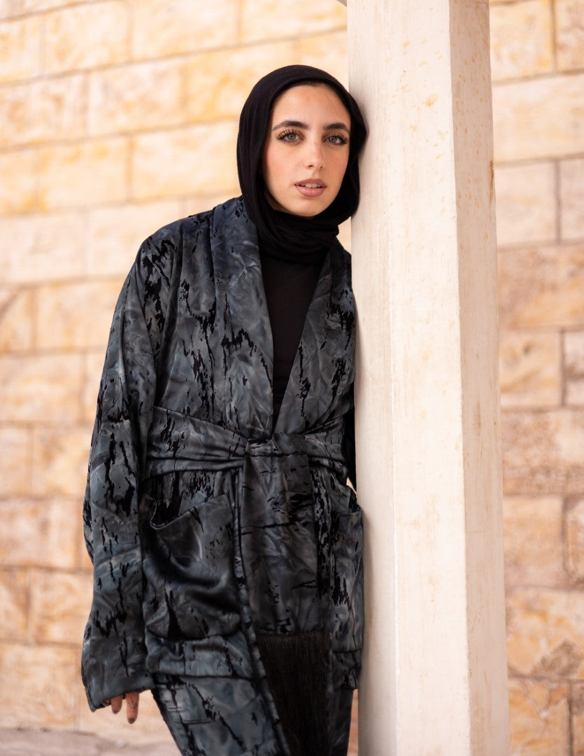 Woman wearing a dark patterned coat against a stone wall.